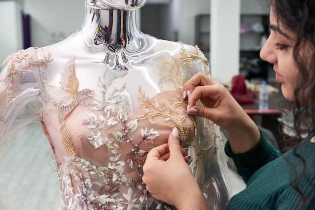 Modista arreglando el vestido de novia de encaje blanco en un maniquí en sastrería