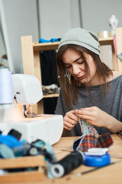 Una modista cose ropa sentada con una aguja en el estudio