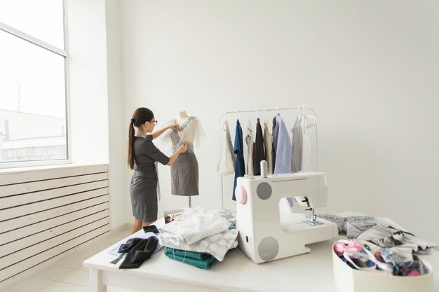 Modista, diseñadora de moda y concepto de sastre: joven y talentosa diseñadora que elige ropa para la nueva colección futura en su propia sala de exposición.