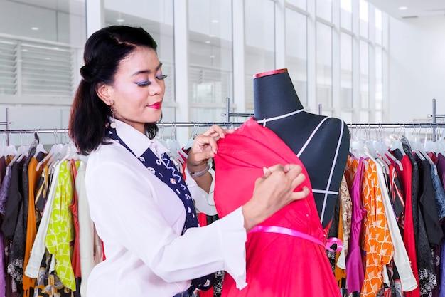 La modista joven ajusta el vestido rojo en un maniquí