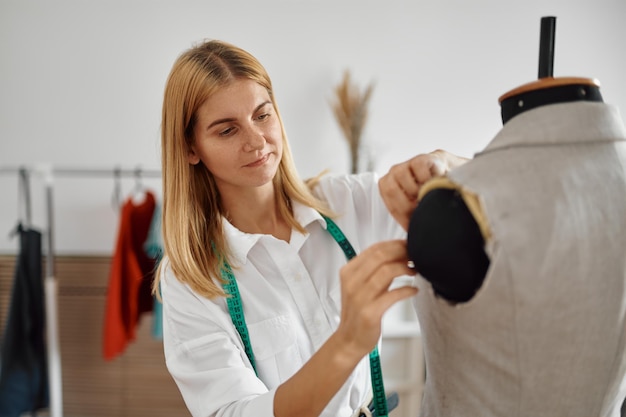 Modista se prueba un vestido en un maniquí en su lugar de trabajo en el taller. Ocupación de corte y confección y costura profesional, negocio de sastrería artesanal, afición artesanal