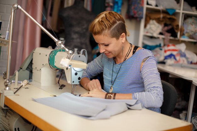 La modista rubia joven trabaja en la máquina de coser. industria de fabricación de vestidos