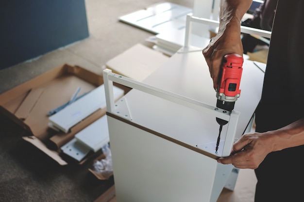 Möbel zu Hause zusammenbauen. Umzug in ein neues Haus oder ein DIY-Konzept. Handwerker, der einen kabellosen Schraubendreher verwendet, um das Gehäuse zu installieren.