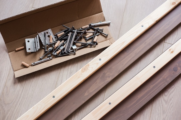 Möbelbeschläge, Schrauben und andere Teile in offener Bastelkiste auf dem Boden liegend, Möbelmontage zu Hause.