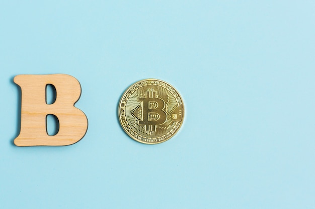 Moeda Bitcoin e ao lado de madeira com a letra B na superfície azul