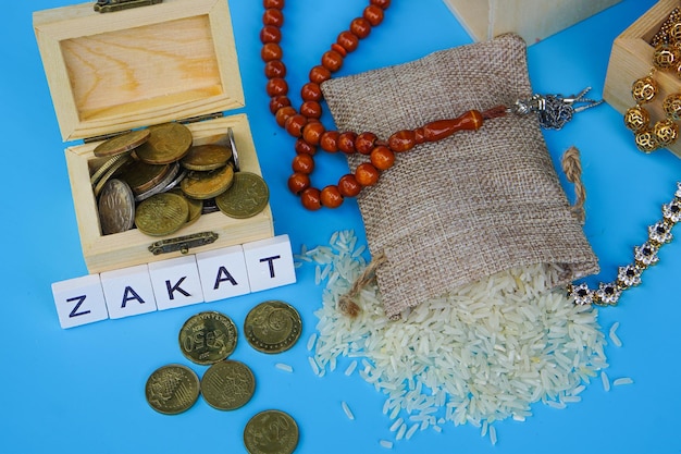 Foto moeda da palavra zakat empilhada de grãos de arroz em uma tigela e mini-casa em fundo azul