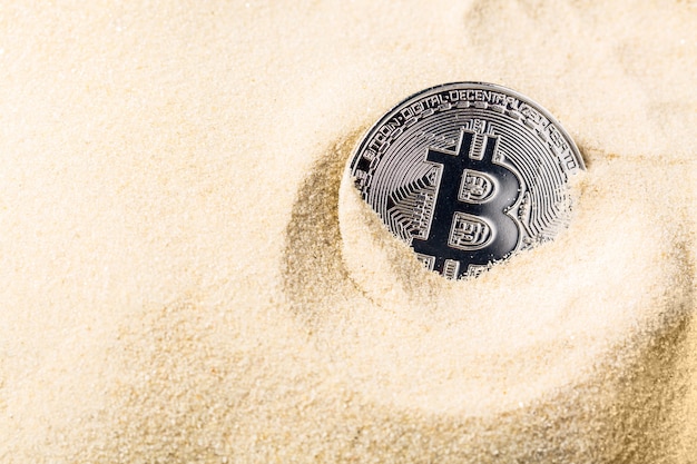 Moeda de Bitcoin afundando na areia.