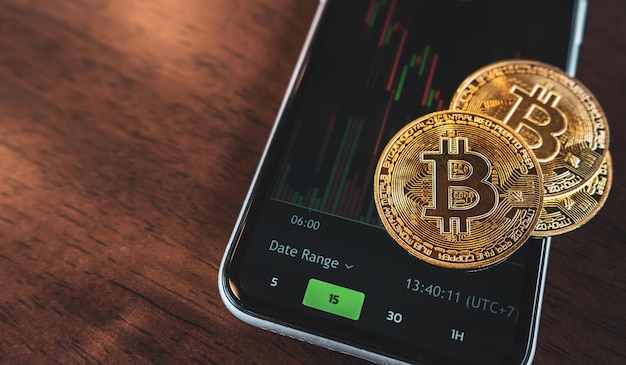 Moeda de ouro Bitcoin colocada em um fundo de telefone celular preto com gráfico de negociação Conceito de criptomoeda