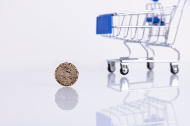 Moeda de um dólar americano no fundo de um carrinho de supermercado em um fundo branco. Copie o espaço. Foco seletivo