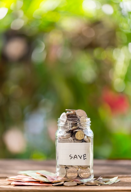 Moedas de depósito de poupança em um frasco de vidro transparente, em um assoalho de madeira com bokeh no backgro