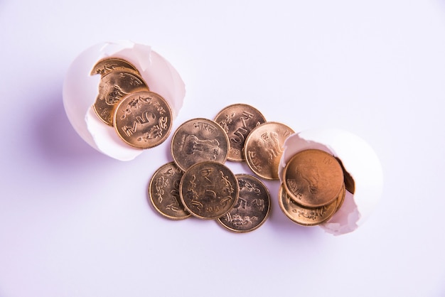 Foto moedas de ouro de cinco rupias indianas emergindo de um ovo quebrado, isoladas sobre um fundo branco