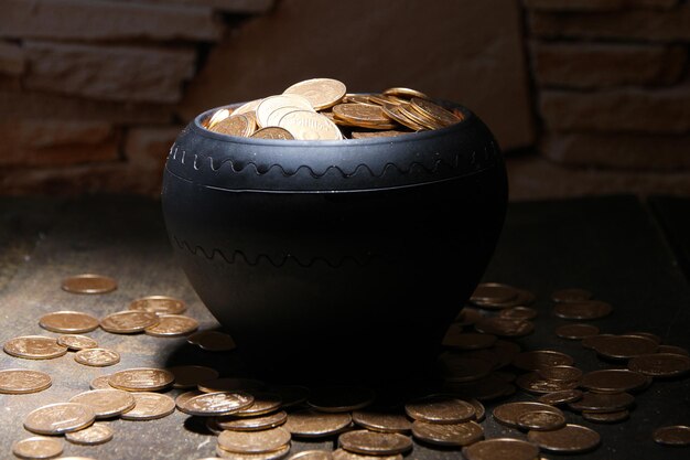 Moedas de ouro em pote de cerâmica na mesa de madeira em fundo escuro