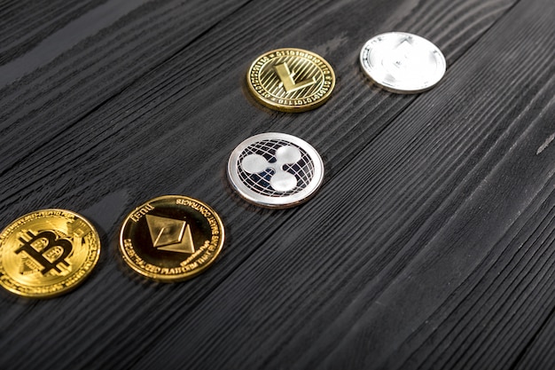 Moedas de prata e douradas com símbolo do bitcoin, da ondinha e do ethereum na madeira.