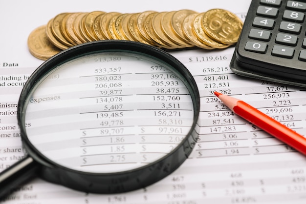 Foto moedas; lupa; lápis e calculadora no relatório financeiro