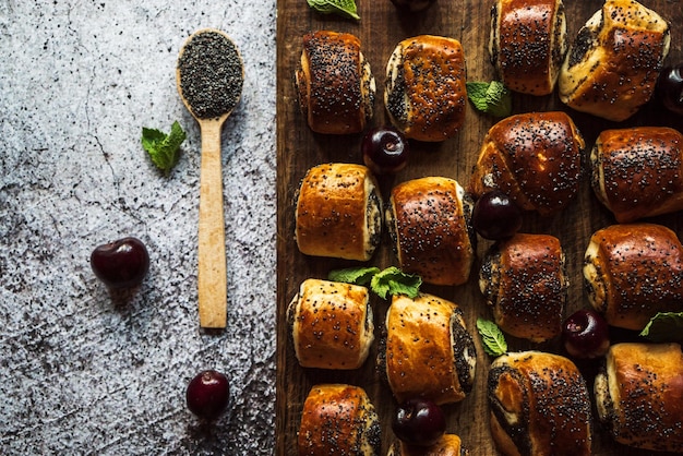 Mohnbrötchen mit Kirschminzblättern und ein Löffel mit Mohn auf einem braunen Holzbrett auf grauem Hintergrund 4