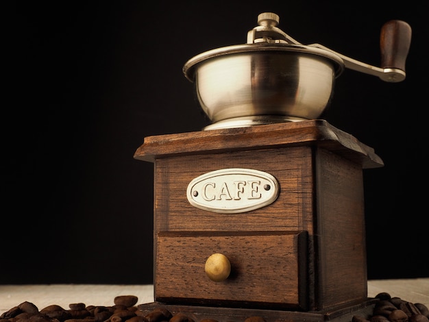 Moinho de moedor de café vintage de close-up com grãos de café sobre um fundo escuro e claro de madeira.