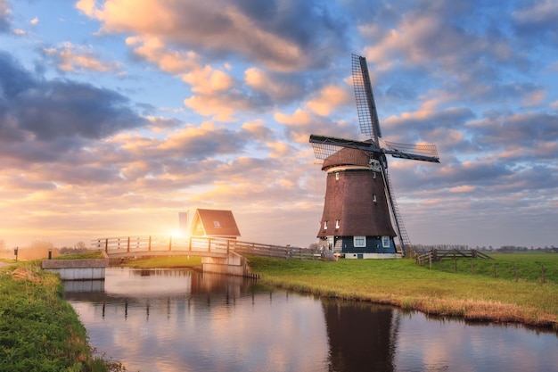 Moinho de vento perto do canal de água ao nascer do sol na Holanda