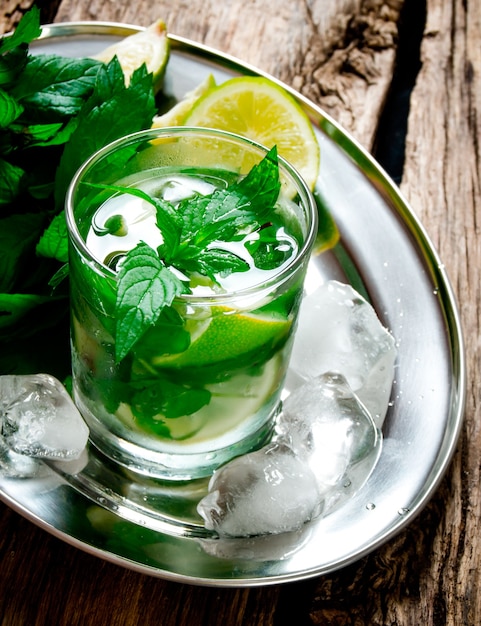 Mojito Cocktail. Frischer Cocktail aus Limette, Minze, Rum und Eis auf einem Metalltablett auf einem Holztisch.