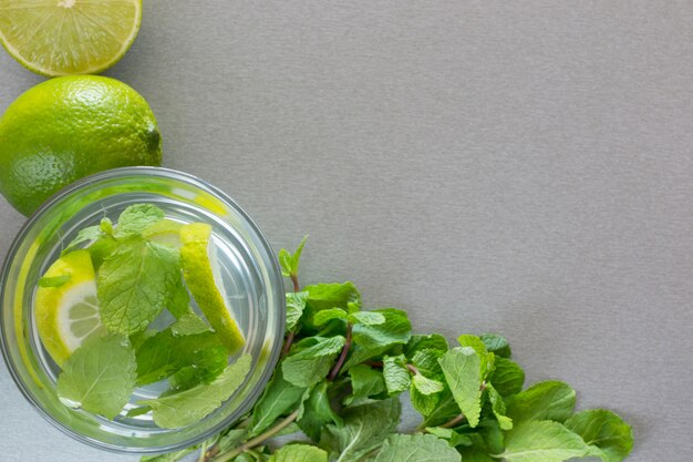 Mojito cocktail con limón y menta en vidrio sobre una pared gris