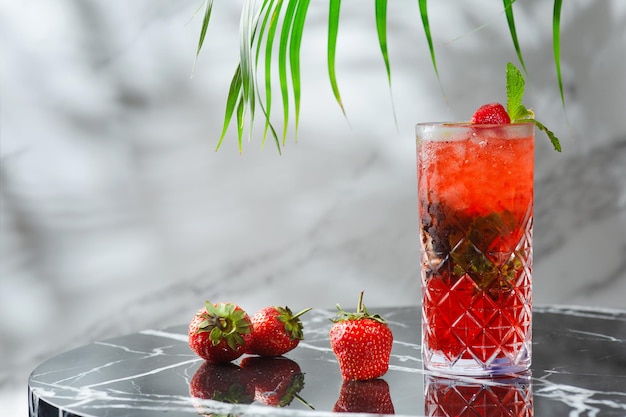 Mojito de fresa con hojas de menta sobre mesa de mármol. bebidas frescas con fresa y rama tropical en el fondo.