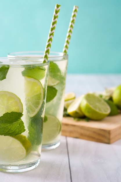 Mojito fresco en vaso con limón y menta en mesa de madera blanca y azul