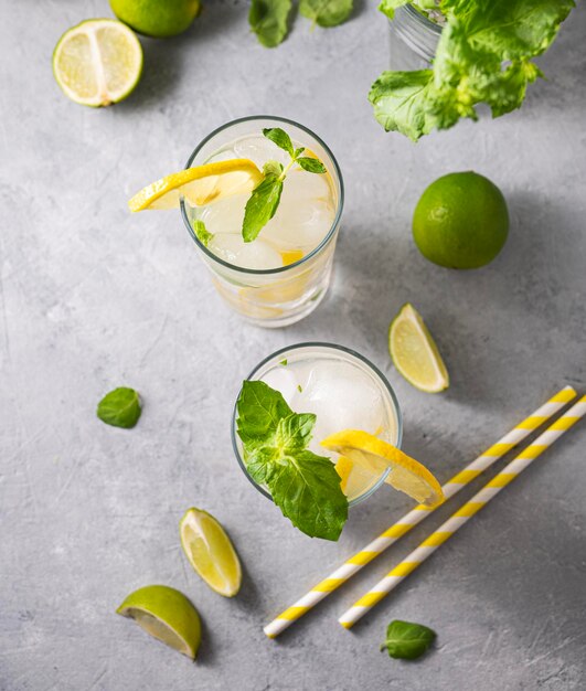 Mojito-Getränk mit frischen Zitronen Erfrischender Cocktail mit Limette, Zitrone, Minze und Eis in einem hohen Glas auf grauem Hintergrund Konzept für kalte Sommergetränke