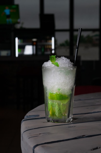 Mojito Long Drink decorado con lima y menta con hielo picado. En una copa de cristal Collins. Sobre un fondo de madera gris. De cerca. Luz dura