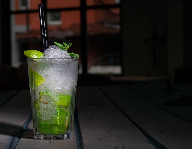 Mojito Long Drink decorado con lima y menta con hielo picado. En una copa de cristal Collins. Sobre un fondo de madera gris. De cerca. Luz dura