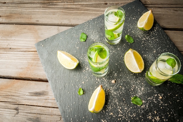 Mojito o limonada con trozos de lima limón hojas de menta sobre un fondo de hormigón negro con hielo c