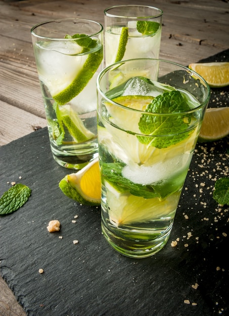 Mojito oder Limonade mit Zitronen-Limetten-Minze-Blättern auf schwarzem Betonhintergrund mit Eis c