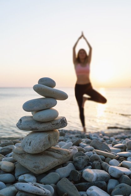 Foto mojón de piedras en la playa con el telón de fondo de una mujer desenfocada haciendo ejercicio vrikshasana