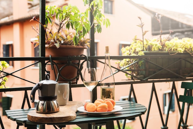 Moka-Kanne, Tasse Kaffee, Aprikosen und eine Flasche Weißwein auf einem kleinen Tisch auf dem Balkon