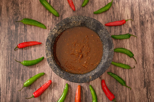 Molcajete mit scharfer Soße auf Holztisch mit Chilischoten drumherum