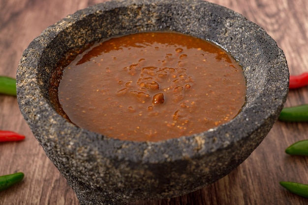 Molcajete mit scharfer Soße auf Holztisch mit Chilischoten drumherum