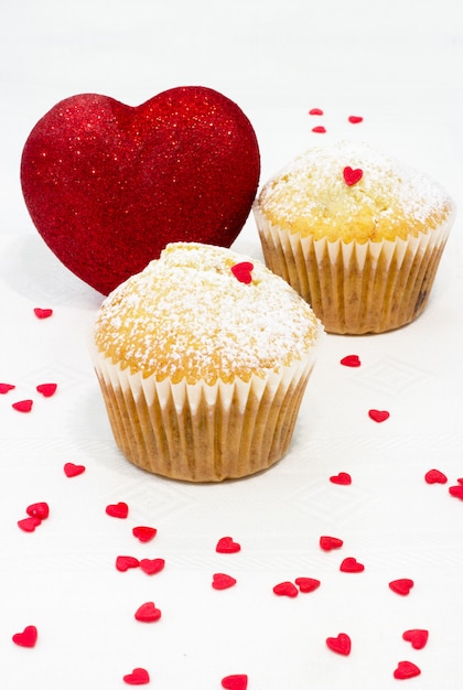 moldes para panecillos en papel, espolvoreados con azúcar glas, corazón rojo brillante y muchos corazones pequeños de azúcar sobre un blanco