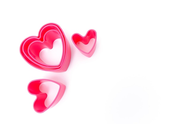 Foto moldes de plástico rosa para hacer galletas en forma de corazones sobre un fondo blanco concepto culinario plano con espacio de copia