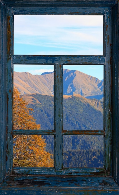 Moldura de janela antiga com restos de tinta azul com uma bela paisagem montanhosa de outono fora da janela