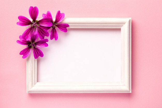 Moldura de madeira branca com flores roxas em fundo de papel rosa.