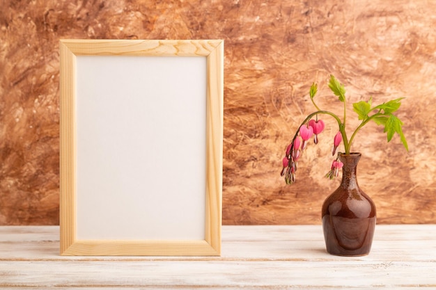 Moldura de madeira com dicentra rosa coração partido em vaso de cerâmica no espaço de cópia de vista lateral de fundo de concreto marrom