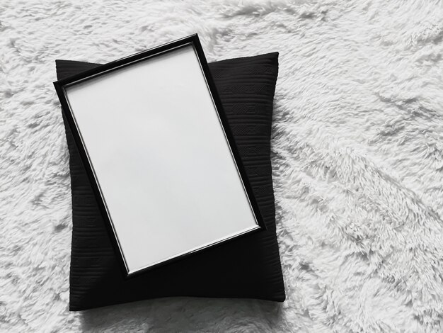 Moldura de madeira fina com copyspace em branco como modelo de impressão de foto de pôster almofada almofada preta e cobertor branco macio plano de fundo e produto de arte vista superior