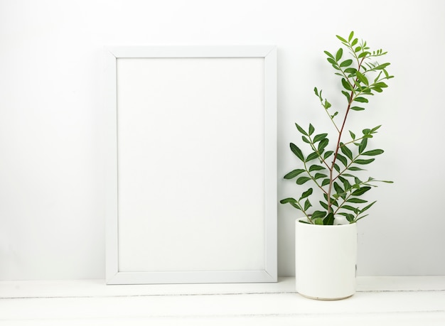 Moldura em branco branca e planta em vaso na mesa de madeira branca