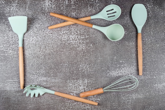 Moldura feita com utensílios de cozinha, utensílios de cozinha doméstica, acessórios de borracha de hortelã em fundo escuro. restaurante, culinária, culinária, tema da cozinha. espátulas e pincéis de silicone, espaço livre para texto.