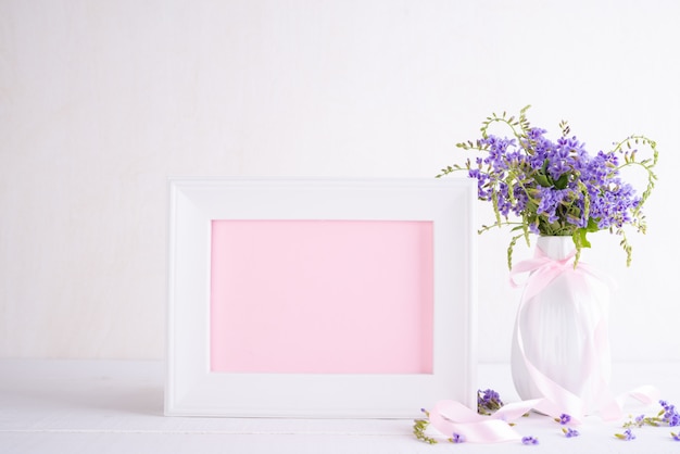 Moldura para retrato branca com a flor roxa bonita no vaso na tabela de madeira branca.