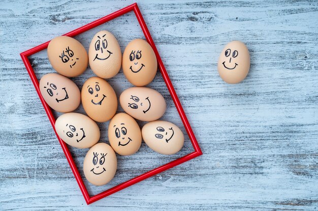 Foto moldura vermelha de imagens e muitos ovos engraçados sorrindo no fundo da parede de madeira branca, close-up. retrato de rosto de emoção de família de ovos. comida engraçada do conceito. copie o espaço