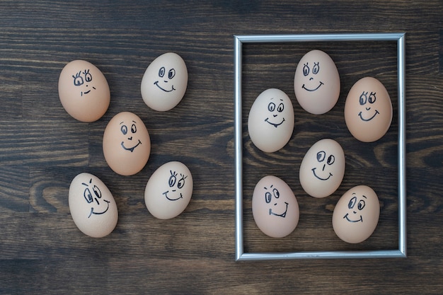 Molduras douradas e muitos ovos engraçados sorrindo no fundo da parede de madeira escura, close-up. Retrato de rosto de emoção família de ovos. Comida engraçada de conceito