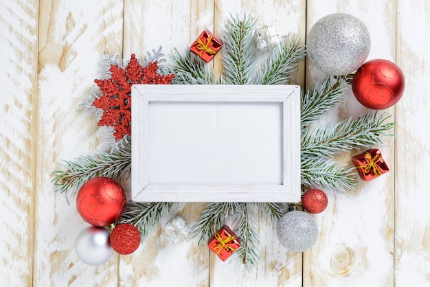Molduras para fotos entre decoração de Natal, com bolas vermelhas e caixa de presente em uma mesa de madeira branca. Vista superior, moldura para copiar o espaço