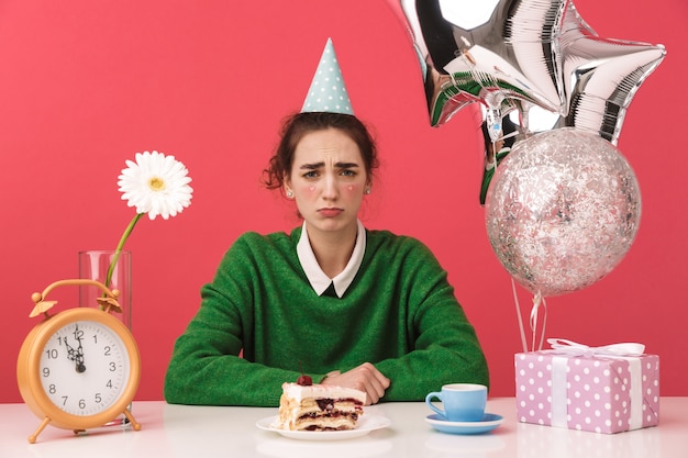 Molesta joven estudiante nerd celebrando su cumpleaños mientras está sentado junto a la mesa y mirando