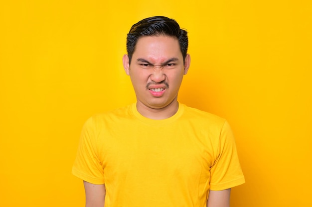 Molesto joven asiático en camiseta casual mirando a la cámara y reaccionando a malas noticias aislado sobre fondo amarillo Concepto de estilo de vida de la gente