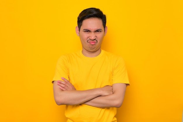Molesto joven asiático en camiseta casual de pie con los brazos cruzados mirando a la cámara aislada sobre fondo amarillo Concepto de estilo de vida de la gente