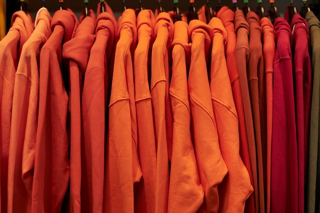 Moletons de cor laranja pendurados em um cabide em uma loja de roupas. Moletons coloridos pendurados em um cabide